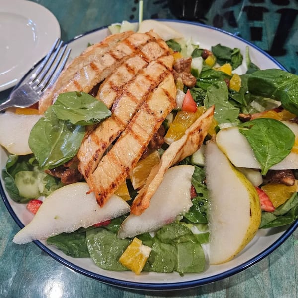 Grilled chicken salad with spinach, pears, oranges, and nuts in a white bowl.