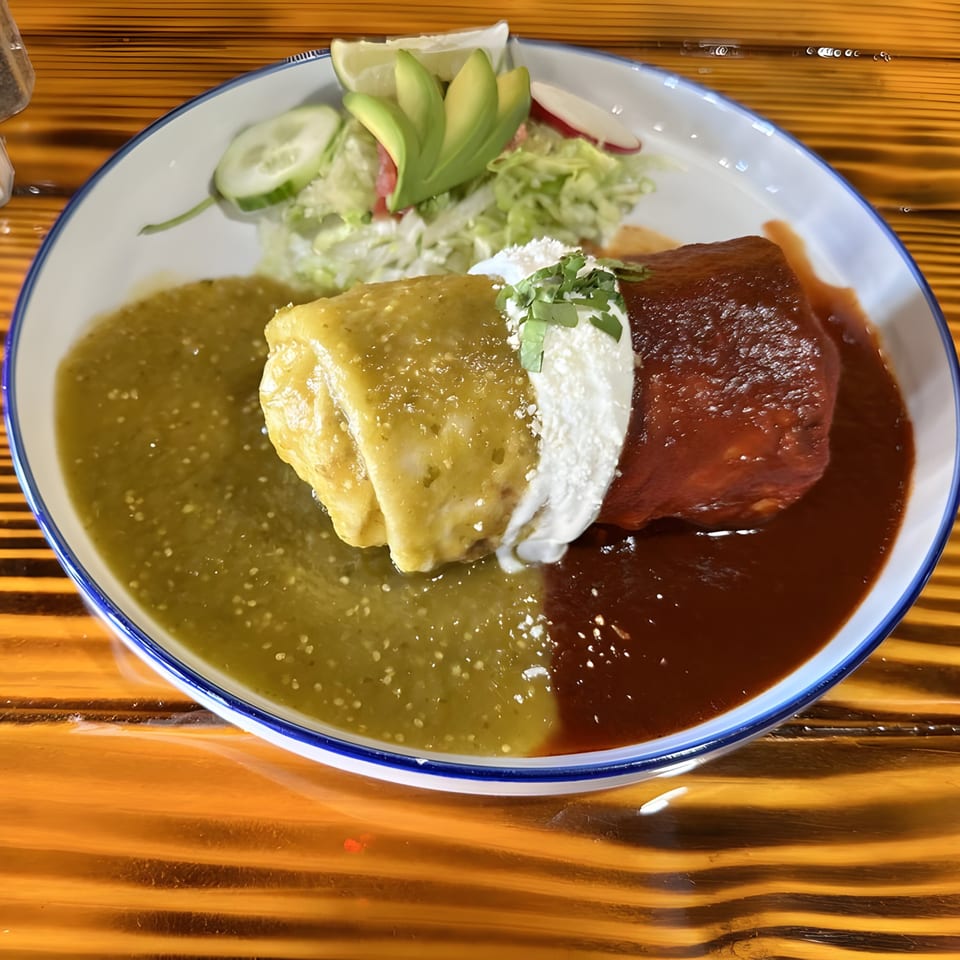 A Mexican burrito covered in green and red sauce, topped with sour cream and cilantro, served with a side salad.